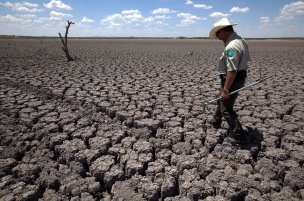 Texas State Park police officer Thomas Bigham walks across the cracked lake bed of O.C. Fisher Lake Wednesday, Aug. 3, 2011, in San Angelo, Texas. A bacteria called Chromatiaceae has turned the 1-to-2 acres of lake water remaining the color red. A combination of the long periods of 100 plus degree days and the lack of rain in the drought -stricken region has dried up the lake that once spanned over 5400 acres. (AP Photo/Tony Gutierrez)