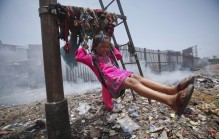 Sana, a 5-year-old girl, plays on a cloth sling hanging from a signalling pole as smoke from a garbage dump rises next to a railway track in Mumbai, India, in 2012.